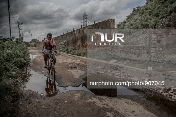 A local man is riding bicycle beside the waste mountain where the road is overflowed by chemical waste water. Dhapa, Kolkata, India. Septemb...