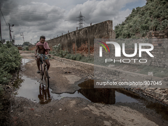 A local man is riding bicycle beside the waste mountain where the road is overflowed by chemical waste water. Dhapa, Kolkata, India. Septemb...