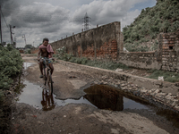 A local man is riding bicycle beside the waste mountain where the road is overflowed by chemical waste water. Dhapa, Kolkata, India. Septemb...