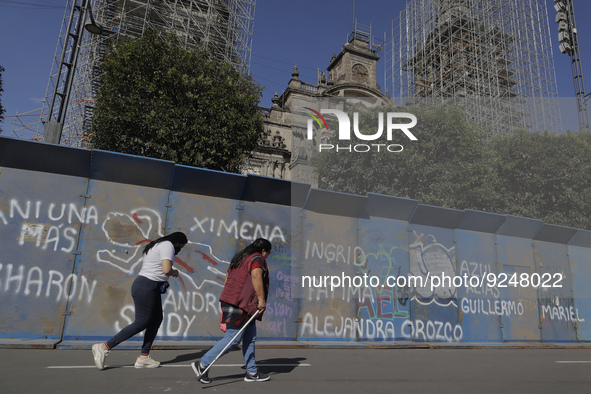 Two women walk in Mexico City's Zócalo in front of metal fences with slogans on the occasion of the International Day for the Elimination of...