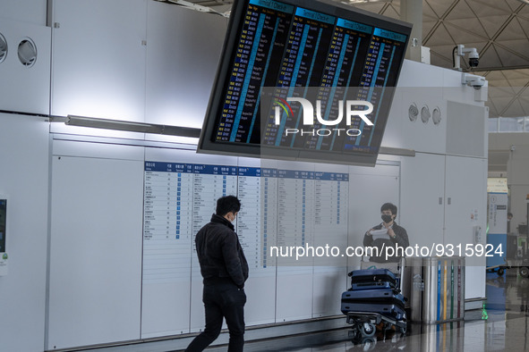 A travellers stands under a flight information display board inside Terminal 1 at Hong Kong International Airport on December 14, 2022 in Ho...