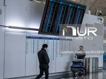 A travellers stands under a flight information display board inside Terminal 1 at Hong Kong International Airport on December 14, 2022 in Ho...