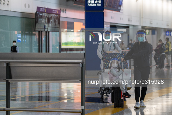 A girl, a woman and a man with luggages wearing a face shield at the arrival hall inside Terminal 1 at Hong Kong International Airport on De...