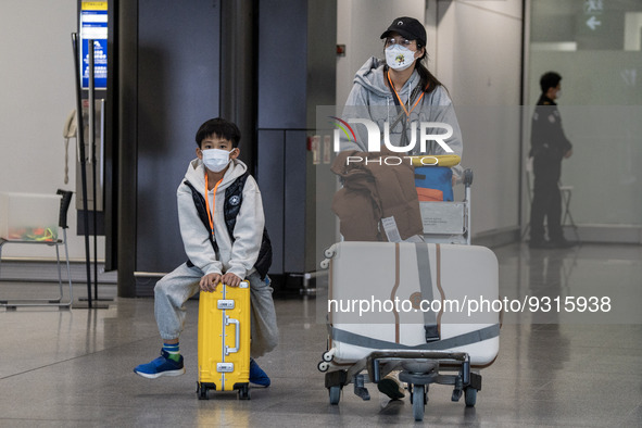 A Boy wearing a face mask sitting on a luggage and a woman pushing a luggage trolley at the arrival hall inside Terminal 1 at Hong Kong Inte...