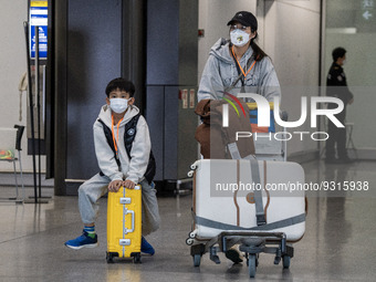 A Boy wearing a face mask sitting on a luggage and a woman pushing a luggage trolley at the arrival hall inside Terminal 1 at Hong Kong Inte...