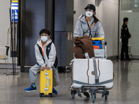 A Boy wearing a face mask sitting on a luggage and a woman pushing a luggage trolley at the arrival hall inside Terminal 1 at Hong Kong Inte...