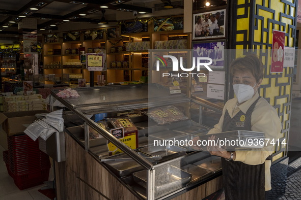 A worker wearing a face mask putting trays on a display counter at a food souvenir store on December 29, 2022 in Macau, China. 