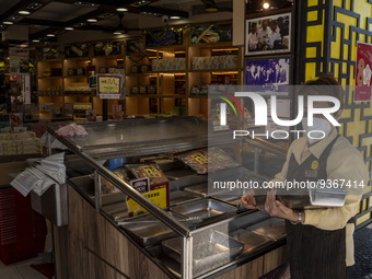 A worker wearing a face mask putting trays on a display counter at a food souvenir store on December 29, 2022 in Macau, China. (