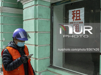 A Delivery worker wearing a face mask looks at his phone while walking pass a for rent sign on a window at an empty store on December 29, 20...