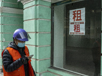 A Delivery worker wearing a face mask looks at his phone while walking pass a for rent sign on a window at an empty store on December 29, 20...