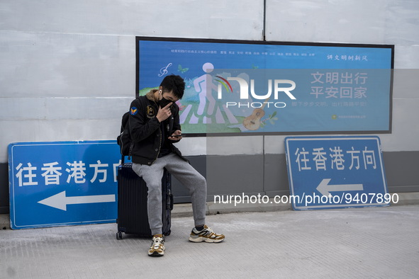 A man sitting on a suitcase next to signs pointing to Hong Kong at Shenzhen Bay Port on January 8, 2023 in Shenzhen, China. Hong Kong today...