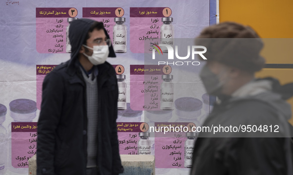 An Iranian worshipper wearing a protective face mask looks on while standing in front of a banner with Images of new coronavirus disease (CO...