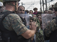 A young migrant looks through the cordon of police, where they are waiting on the Macedonian-Greek border where they are being held, since M...