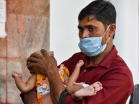 

A father is seen holding a napkin to his child's forehead, who is suffering from fever, in front of the emergency ward of a government-run...