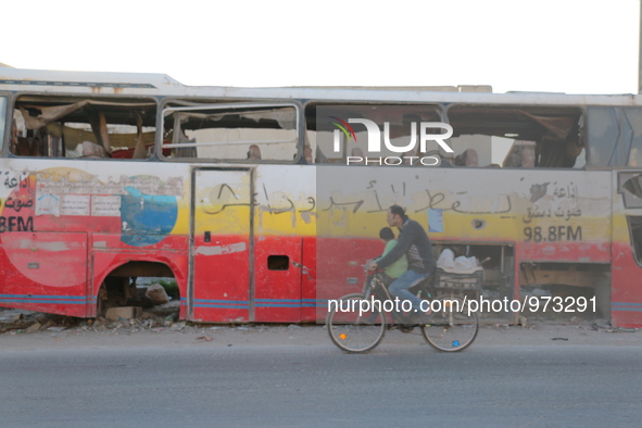 A Syrian man rides a bicycle  past a damaged bus in the Al-Sakhour neighbourhood of Aleppo on December 24, 2015. The graffiti on the bus rea...